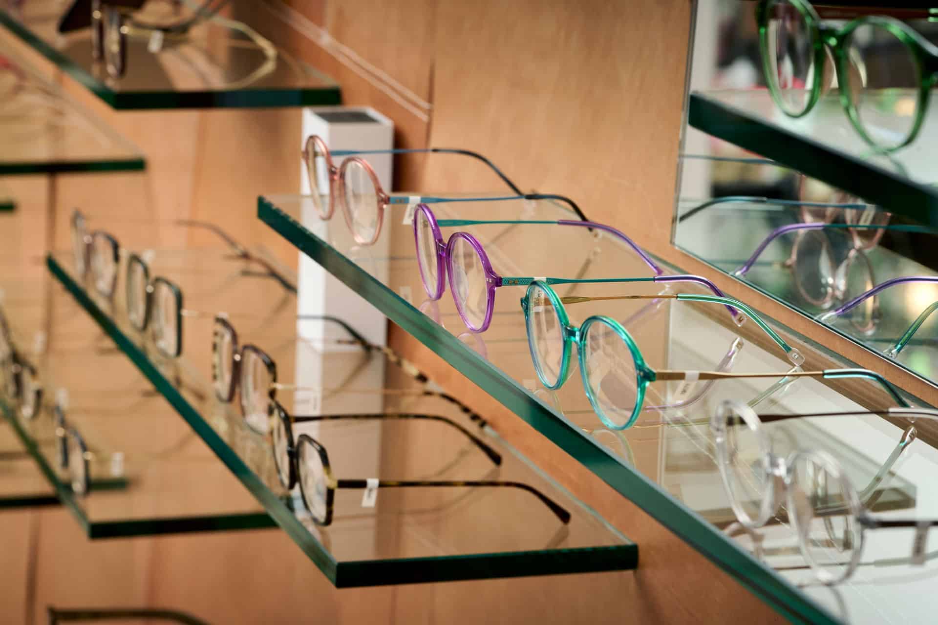 Nærbillede af farverige brillestel udstillet på glashylder hos No. 1 Optik